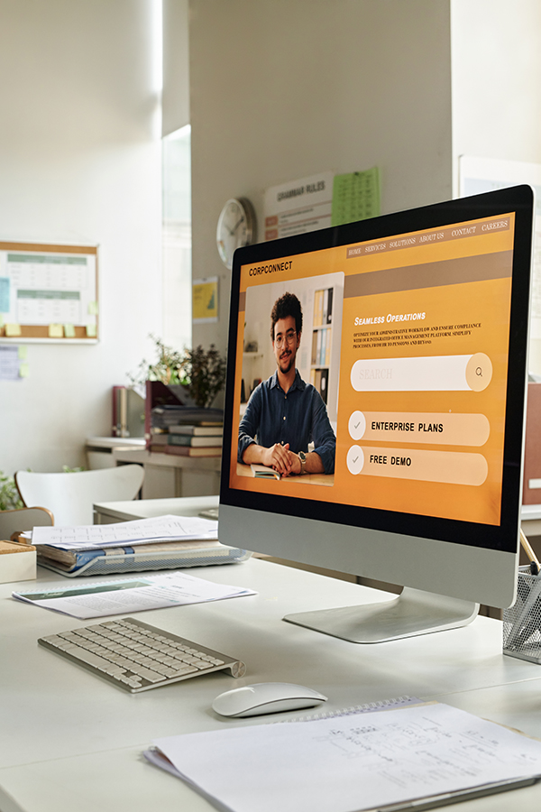 Person working in modern office setting, focused on computer screen displaying business software. Multiple documents and office supplies scattered on desk