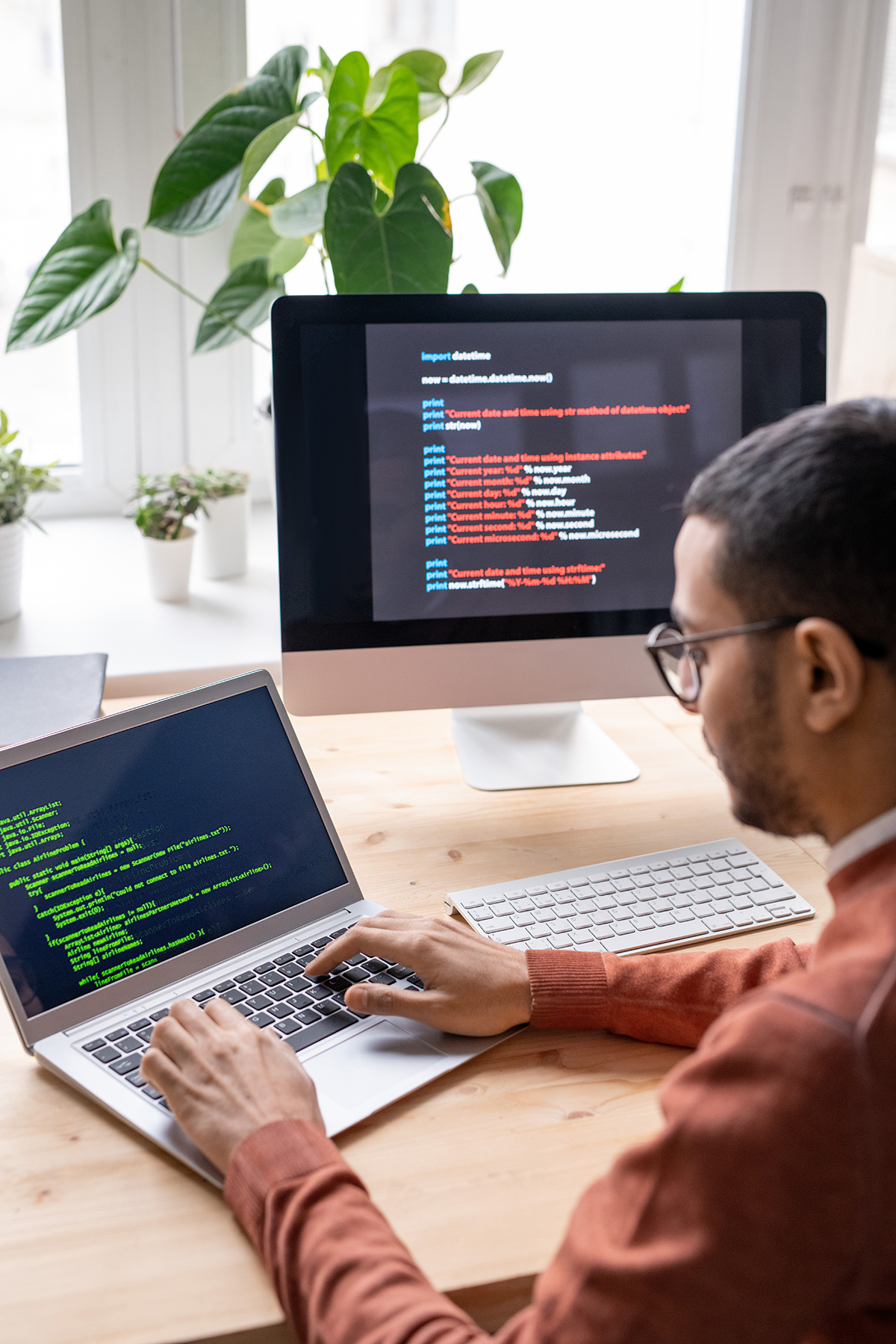 Over shoulder view of young web developer sitting at desk and working with laptop while creating computer algorithm